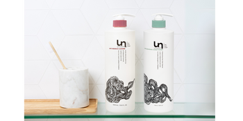 Unwash liter-size shampoo and cleansing conditioner bottles on a glass shelf in a modern bathroom, designed for hydration, balance, and better haircare value.